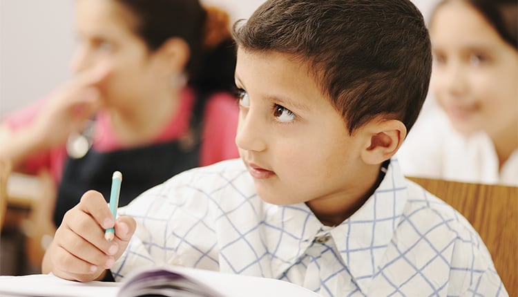 young boy takes notes in elementary school classroom