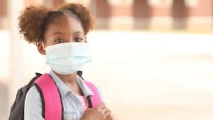 School-age girl in face mask getting ready for first day of school
