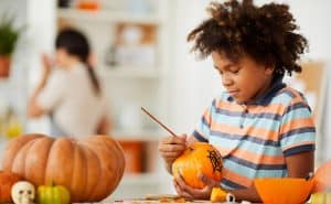 Child painting pumpkins for Halloween as their parent works on other crafts in background