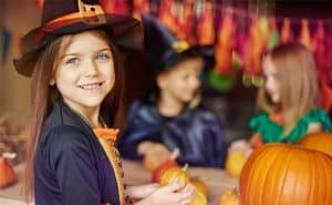Girl in witch costume making crafts with pumpkins for Halloween