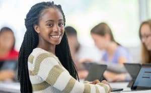 A girl smiles. She is in a classroom with laptops.