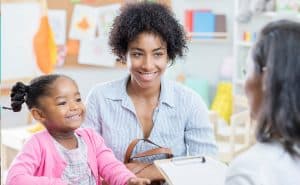A family meets with their child's teacher. Using a two generation approach means educators can work to address the needs of a child's family at home, leading to success in school.