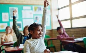 A confident girl raising her hand in the classroom.