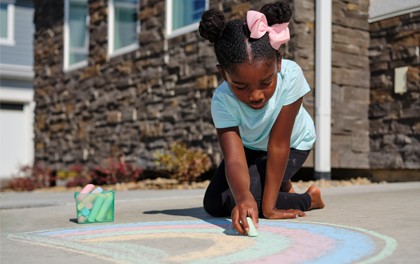 A girl plays with sidewalk chalk outside.