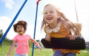 Two girls play outside on swings together.