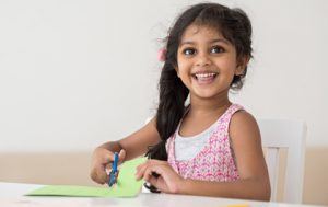 A young girl uses scissors to cut construction paper