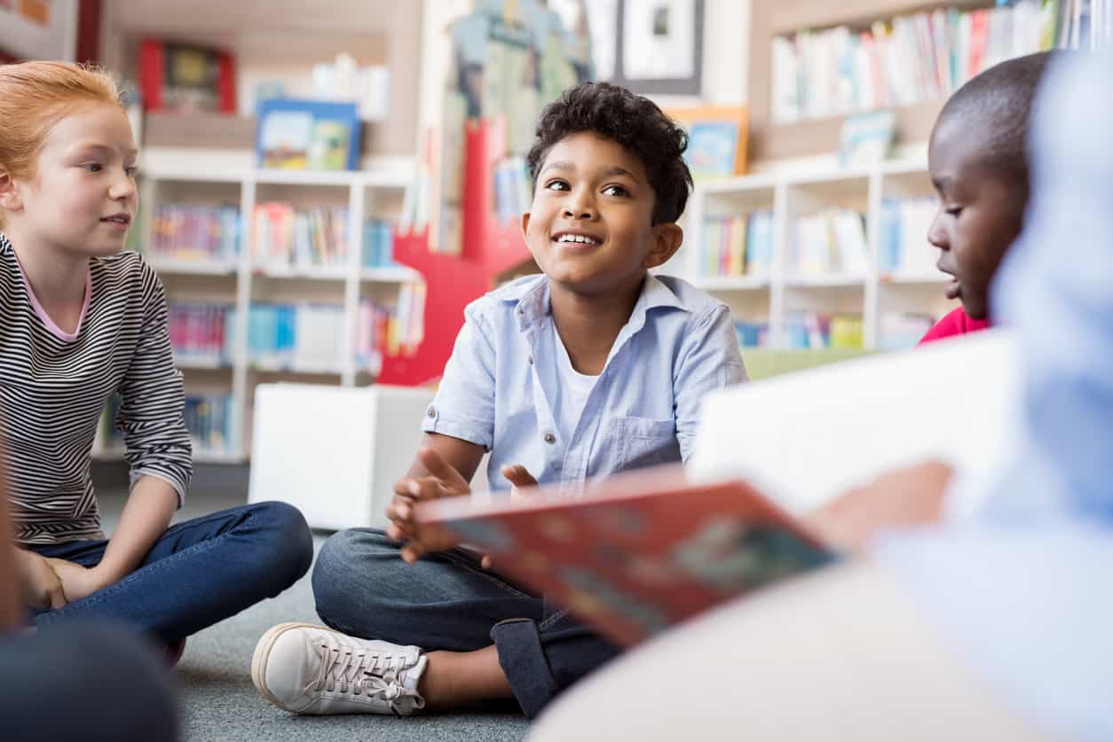 group of kids sitting on floor in circle around the teacher and listening a story