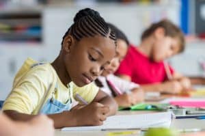 Pupil writing at desk in classroom at the elementary school. Student girl doing test in primary school. Children writing notes in classroom. African schoolgirl writing on notebook during the lesson.