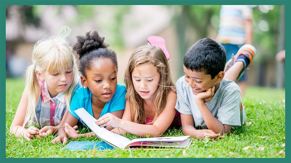 4 children looking over a book, in the grass