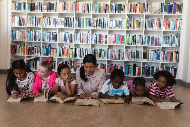 Female-teacher-and-schoolkids-reading-a-book-while-lying-on-floor-of-school-library-1126246072_2125x1416.jpeg